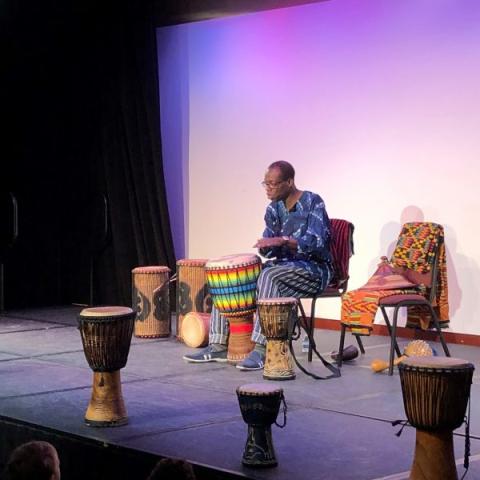 Kofi Dennis on stage with West African drums.